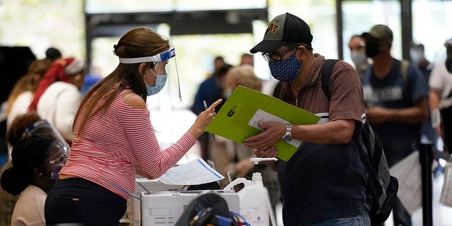 An election worker, left, gives instructions for voting at an early voting site, Monday, Oct. 19, 2020, in Miami. (AP Photo/Lynne Sladky)