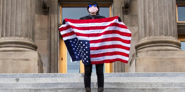 A student holding a U.S. Flag upside down stands atop the steps at the Idaho Capitol Building Monday, April 26, 2026 in Downtown Boise. (Darin Oswald /Idaho Statesman via AP)