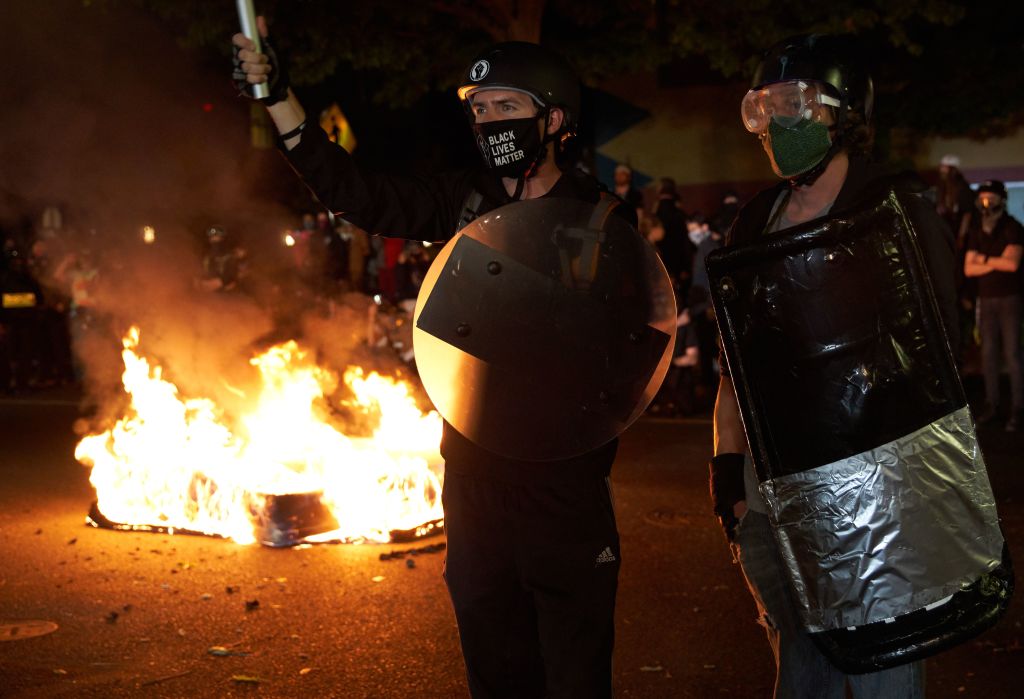 Protestors stand as mattresses are set on fire in front of the North Precinct Police building in Portland, Oregon on September 6, 2020. - Protestors are marching for an end to racial inequality and police violence. Aaron Danielson, 39, a supporter of a far-right group called Patriot Prayer, was fatally shot August 29, 2020, in Portland, Oregon after he joined pro-Trump supporters who descended on the western US city, sparking confrontations with Black Lives Matter counter-protesters. (Photo by Allison Dinner / AFP) (Photo by ALLISON DINNER/AFP via Getty Images)